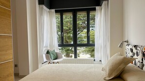 Un dormitorio con una cama grande, una silla y un ventanal con cortinas.