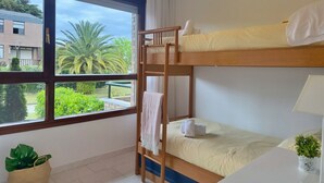 Une chambre avec des lits superposés donnant sur un bâtiment et sur la verdure environnante.