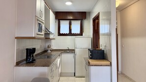 Une cuisine compacte avec des meubles blancs, un four à micro-ondes, un réfrigérateur, une machine à café et un grille-pain.
