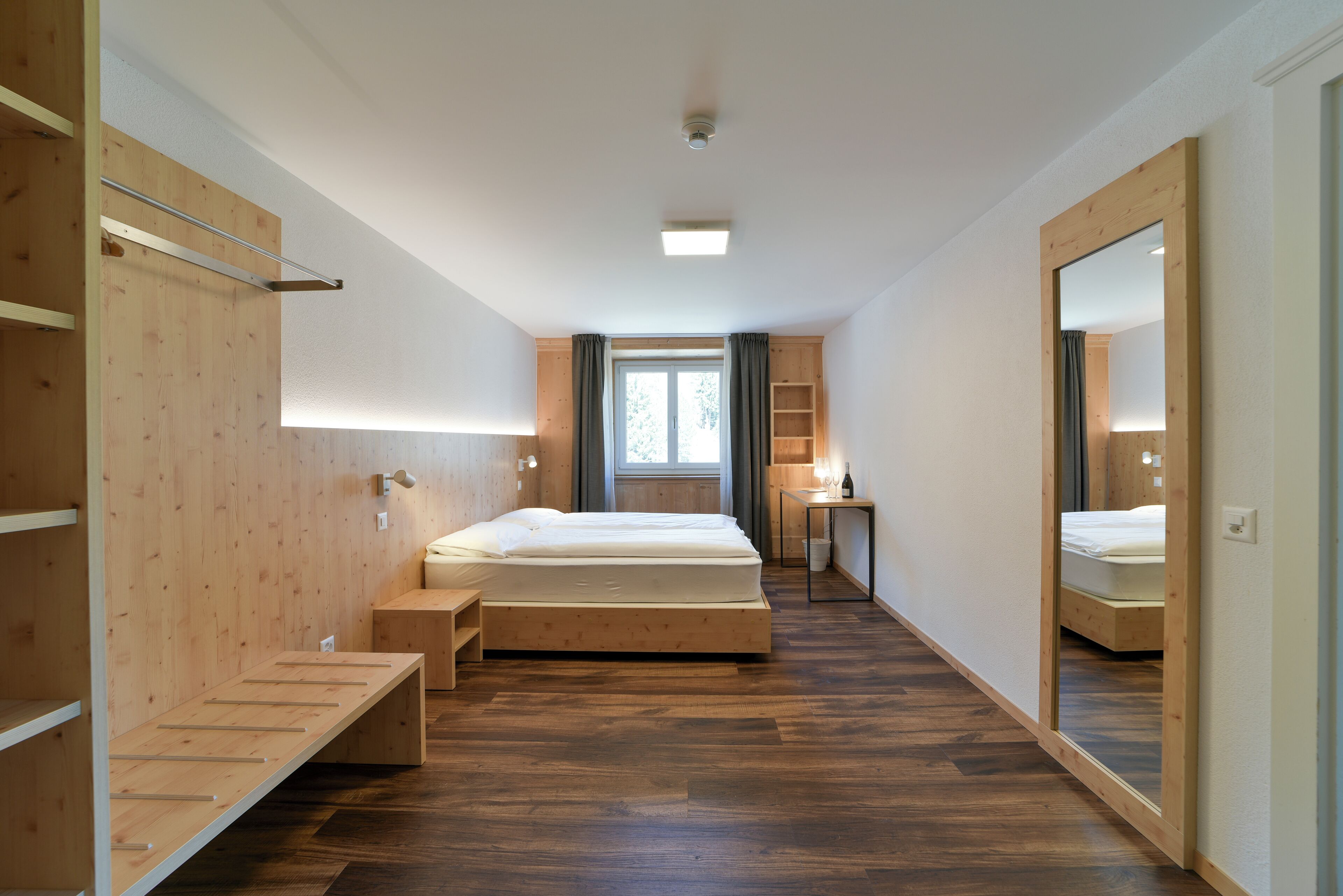 A modern bedroom with a wooden floor, a single bed, a desk, and a large mirror.