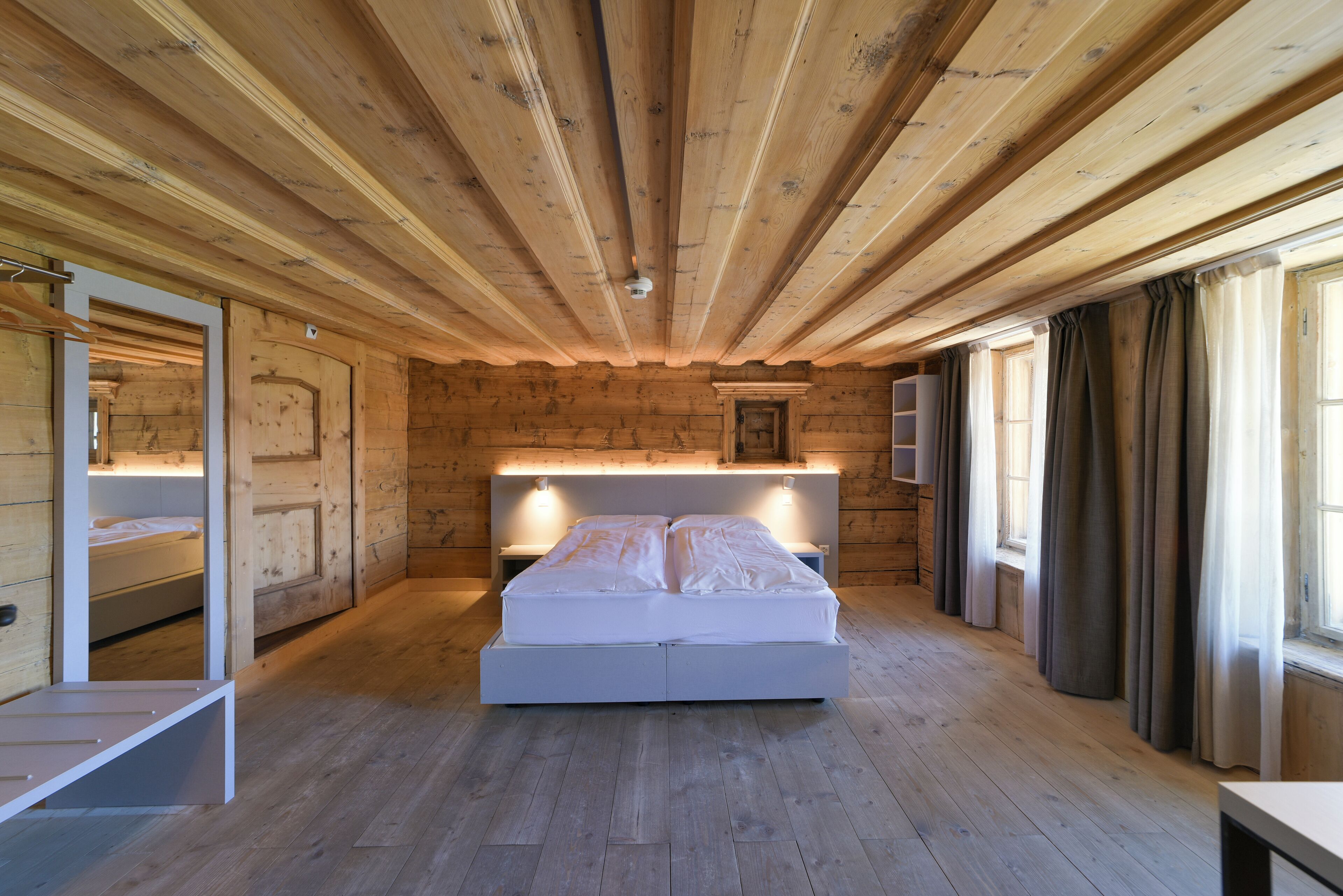 Un dormitori de cabana de fusta amb un llit, taules de nit i una finestra amb cortines.