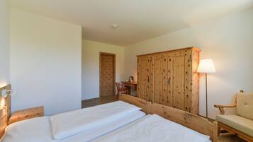 Un dormitorio con dos camas, un armario de madera, un escritorio con silla y una lámpara.