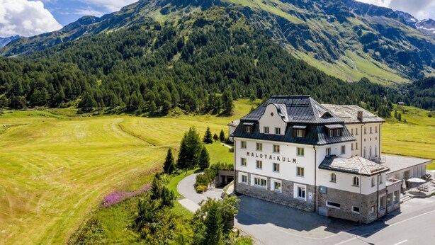 Een hotel in traditionele Europese stijl, omringd door weelderige groene velden en een bergpanorama.