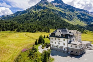 Ein Hotel im traditionellen europäischen Baustil, umgeben von üppigen grünen Feldern und einem Bergpanorama.