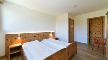 Una habitación con una cama de madera, mesitas de noche, una silla y una puerta.