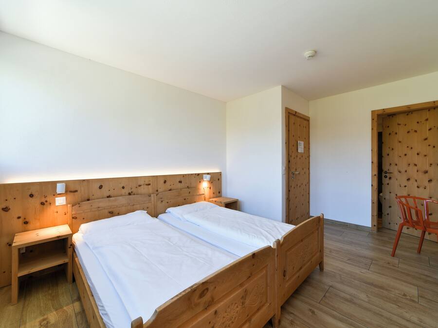 Una habitación con una cama de madera, mesitas de noche, una silla y una puerta.