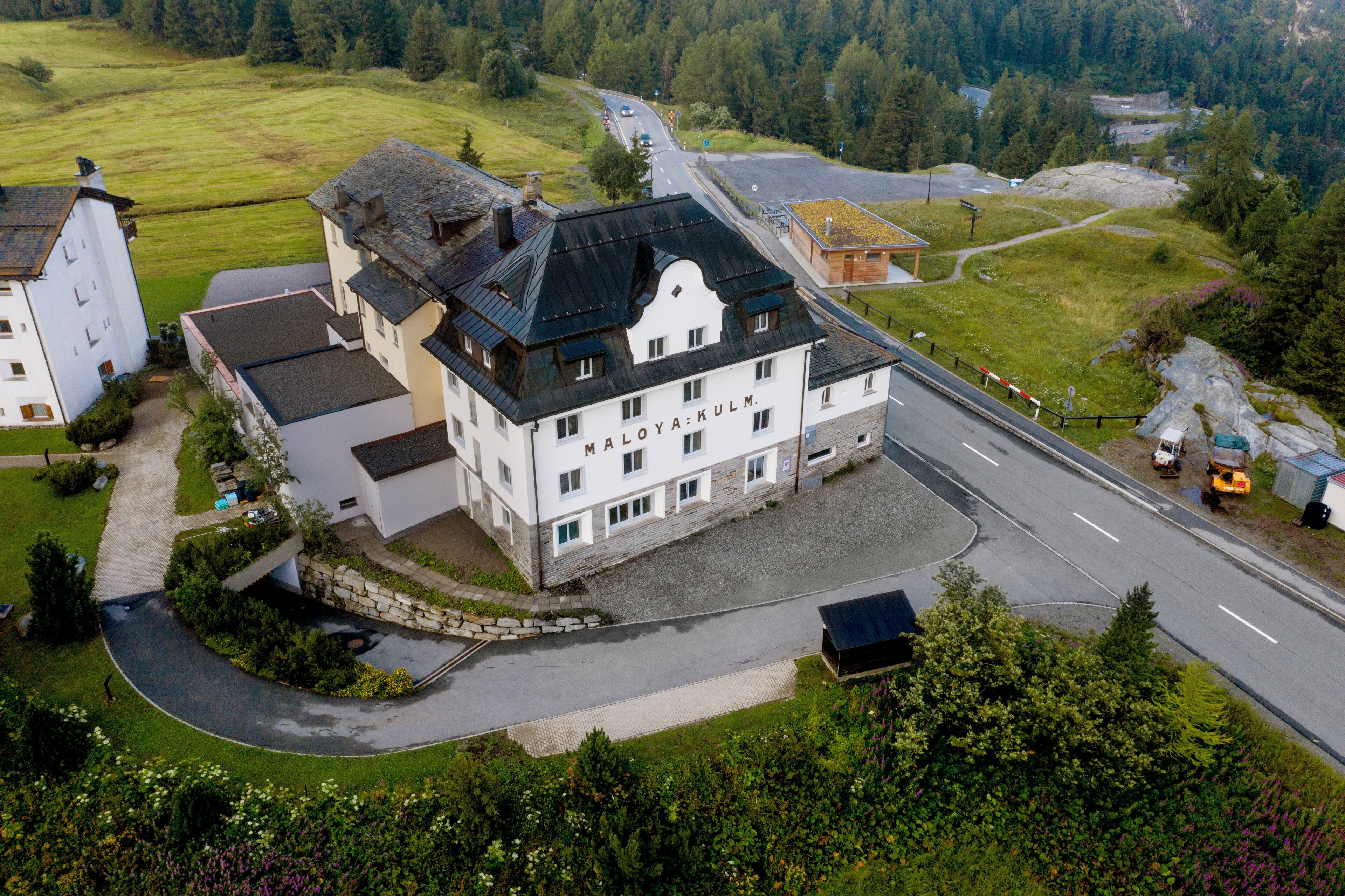 A large, white building with a black roof, surrounded by a well-maintained lawn and a road.