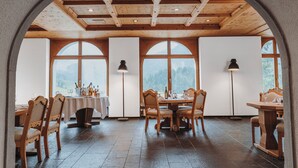 Een eetruimte met houten tafels en stoelen, grote gewelfde ramen en een rustiek plafond.