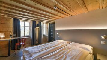 A wooden cabin room with a bed, desk, chair, and a window with curtains.