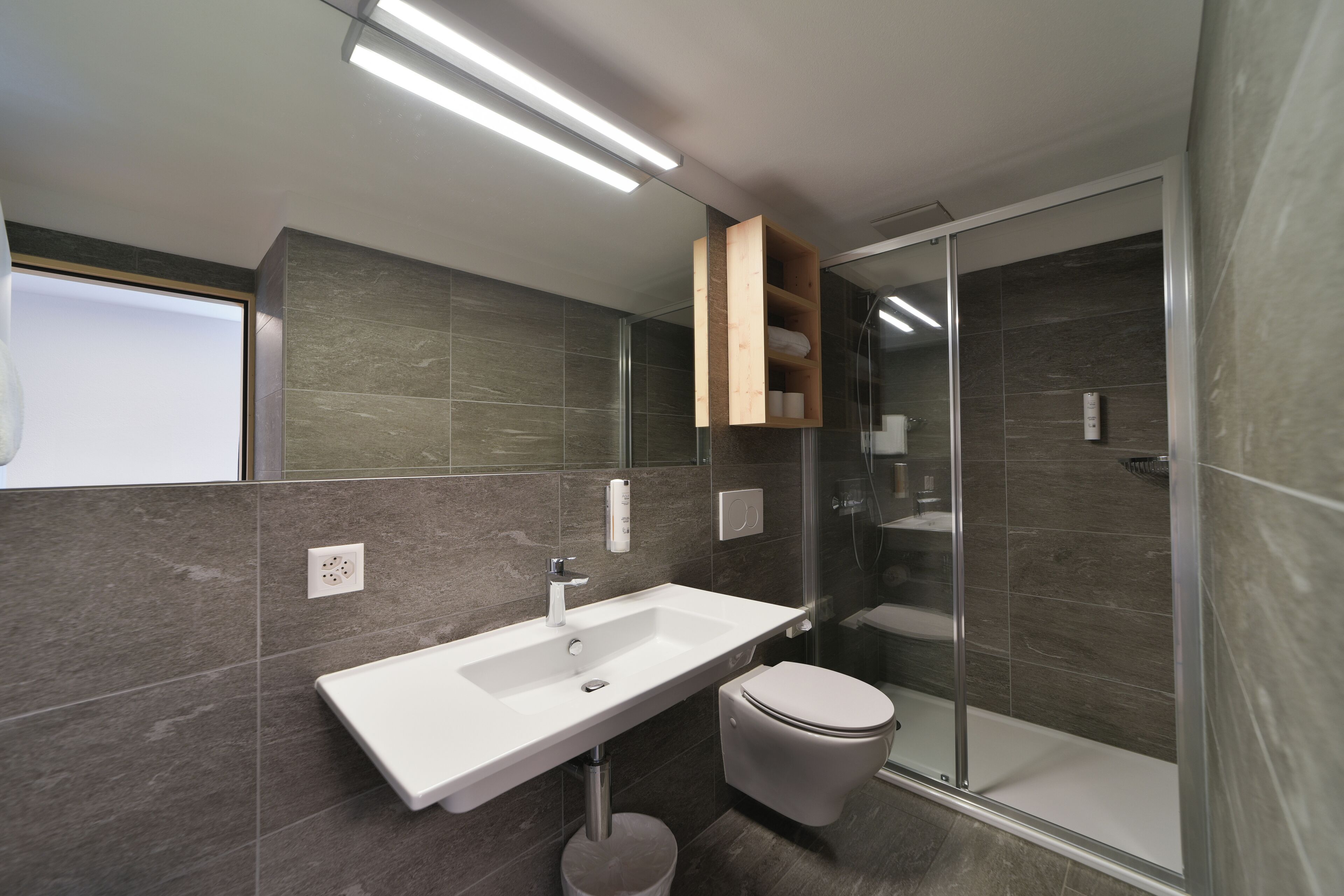A modern bathroom with a white sink, a toilet, and a glass-enclosed shower.