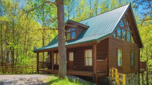 A cabin with a porch, large windows, and a stone foundation. - SkiView Hilltop: Honeymoon, Hot Tub, Wifi, Wooded View, Great Location! (Sevierville)