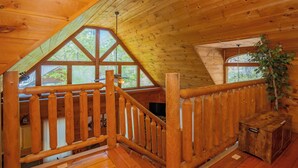 A wooden cabin with a loft bedroom, a wooden staircase, and a large window overlooking greenery. - SkiView Hilltop: Honeymoon, Hot Tub, Wifi, Wooded View, Great Location! (Sevierville)
