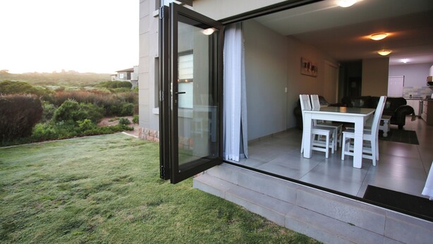 A modern house with a glass door leading to a dining area with a table and chairs. - Francolin's Nest, Langebaan, 4-sleeper (Langebaan)