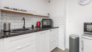 A modern kitchen with white cabinets, a black countertop, a sink, a kettle, a microwave, and a trash bin. - Z widokiem na sopot by Grand Apartments (Sopot)