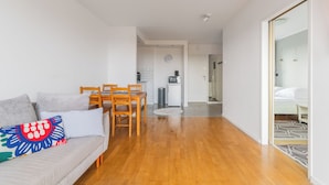 A modern living room with a sofa, wooden dining table, and chairs. A kitchen with a microwave and sink is visible in the background. - Z widokiem na sopot by Grand Apartments (Sopot)