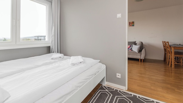 A bedroom with a bed, a window with curtains, a small table, and a sofa in the adjacent room. - Z widokiem na sopot by Grand Apartments (Sopot)