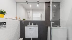 A modern bathroom with a white sink, dark wall, and a glass shower enclosure. - Z widokiem na sopot by Grand Apartments (Sopot)