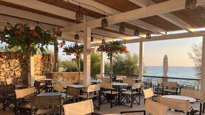 An outdoor patio with tables and chairs, stone walls, hanging plants, and a view of the sea. - Moya Boutique Sleep (Drvenik Mali)