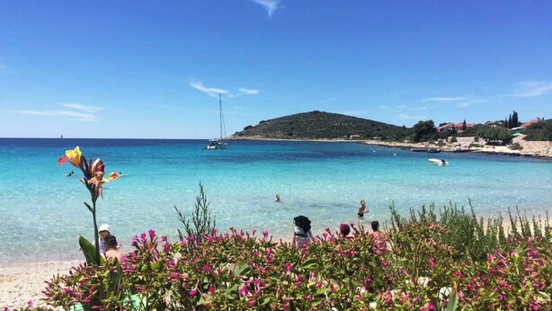 A beach with clear turquoise water, a sailboat, and a small hill in the background. - Moya Boutique Sleep (Drvenik Mali)