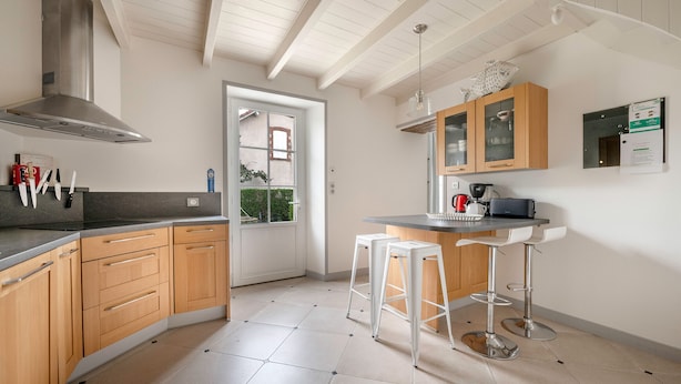 Cocina moderna con gabinetes de madera, campana extractora de acero inoxidable y una barra con taburetes.
