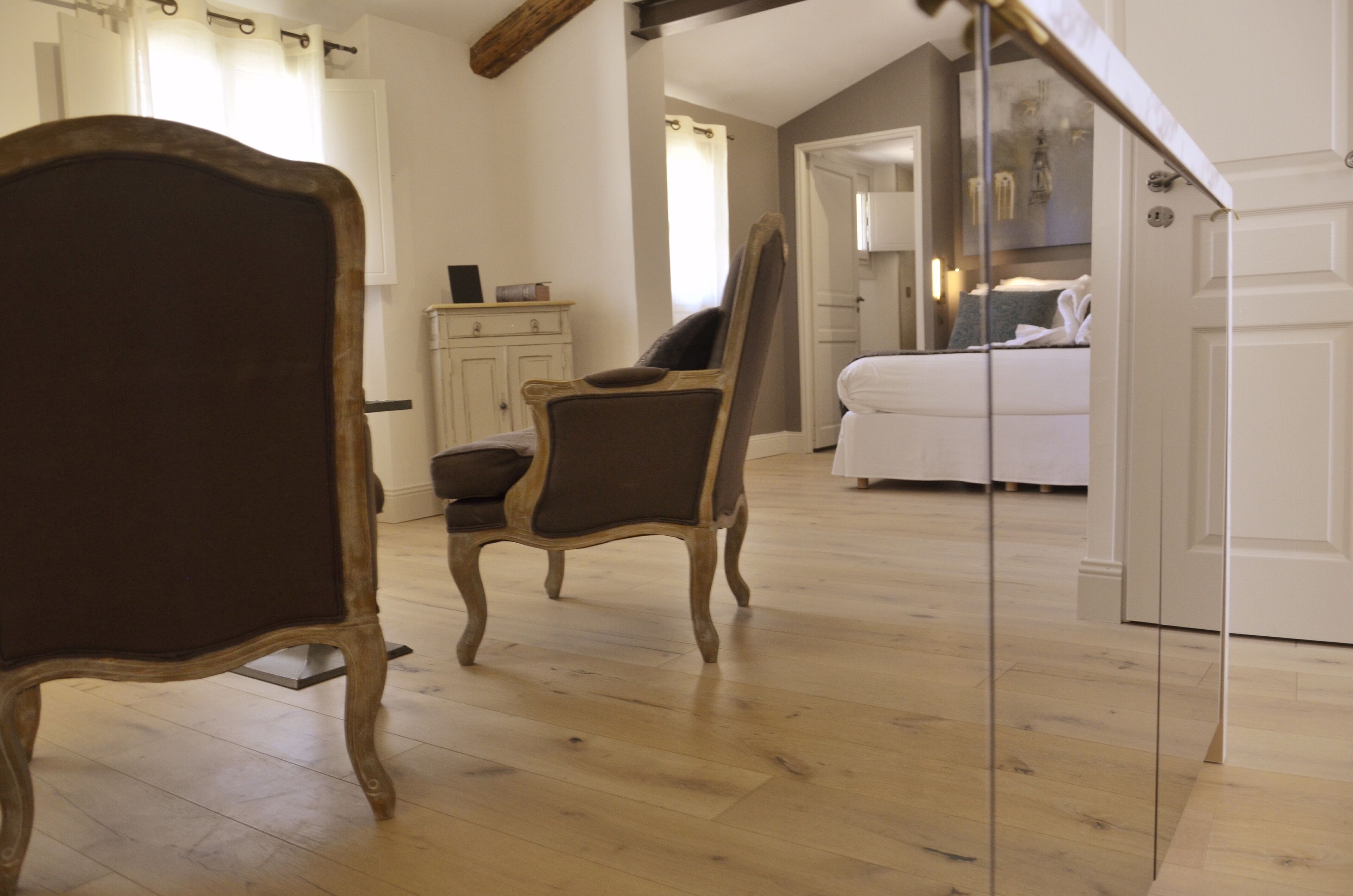 Una habitación con piso de madera, una cama con ropa de cama blanca, una silla y un armario.