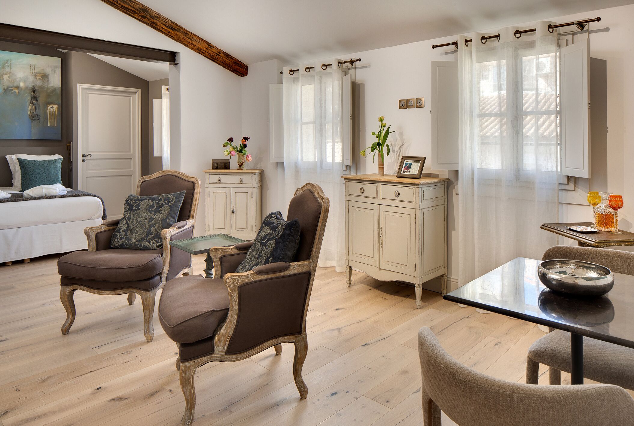 A cozy room with a bed, two armchairs, a dining table, and a cabinet.