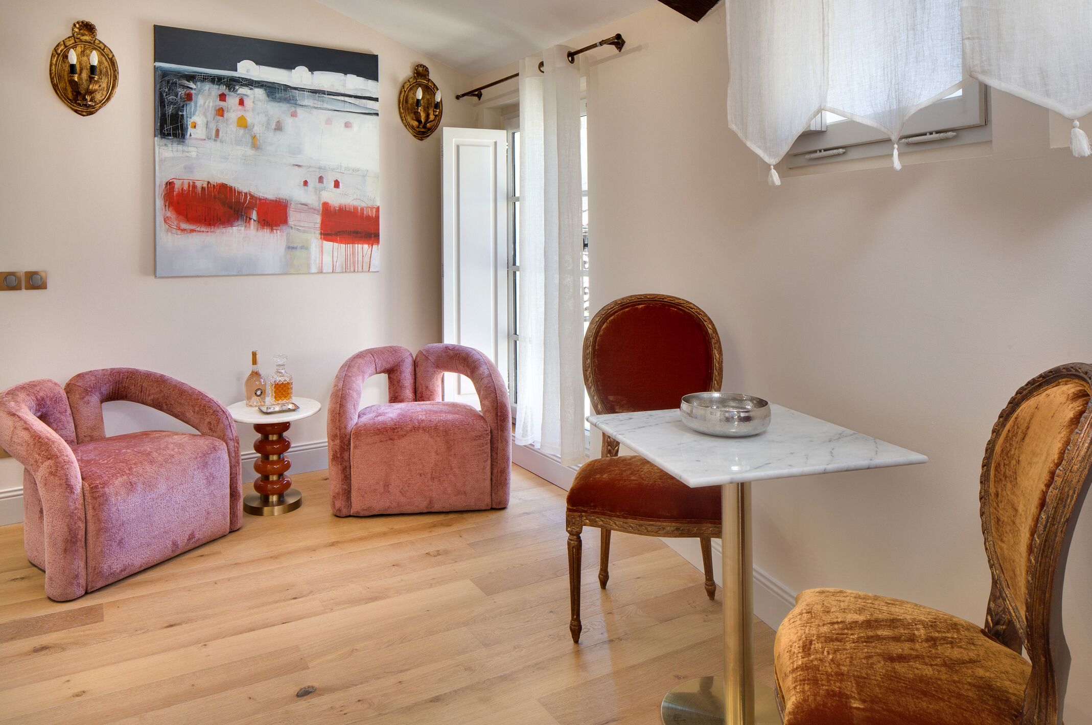 Een kamer met twee roze fauteuils, een houten stoel, een kleine tafel met een schaal en een schilderij aan de muur.
