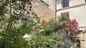 A garden with various plants and flowers, including roses and bougainvillea, in front of a building with a stone wall and a statue. - Cloître des Augustins 5 étoiles, Spa & Fitness (Avignon)