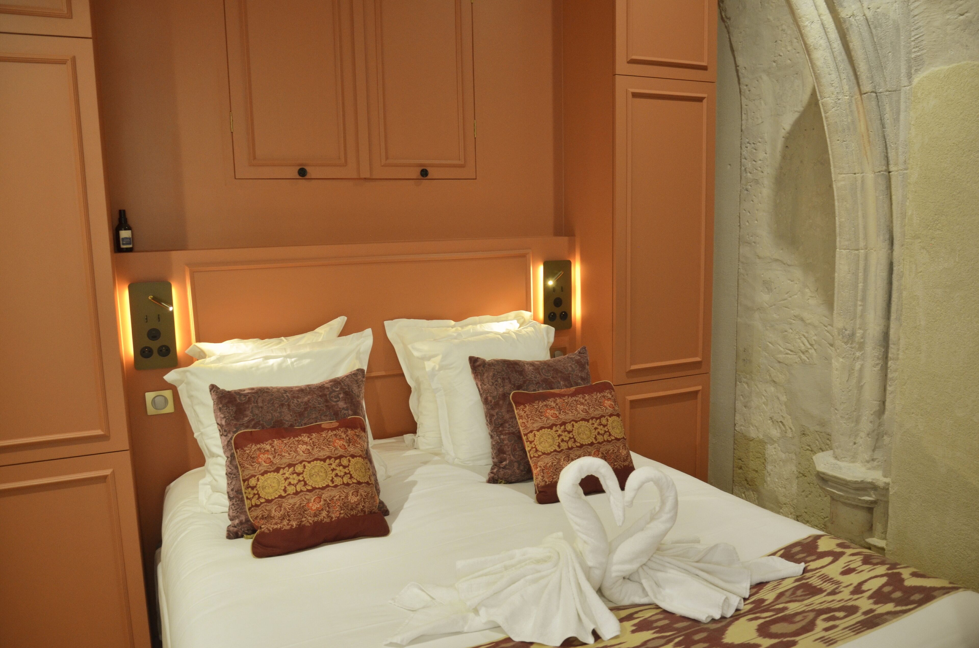 A neatly made bed with pillows and a towel, a wall clock, and a thermostat on the wall.
