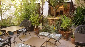 Un patio al aire libre con mobiliario de mimbre, plantas en macetas y una fuente de piedra.