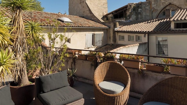A rooftop terrace with wicker furniture, potted plants, and a view of a historic tower. - Cloître des Augustins 5 étoiles, Spa & Fitness (Avignon)