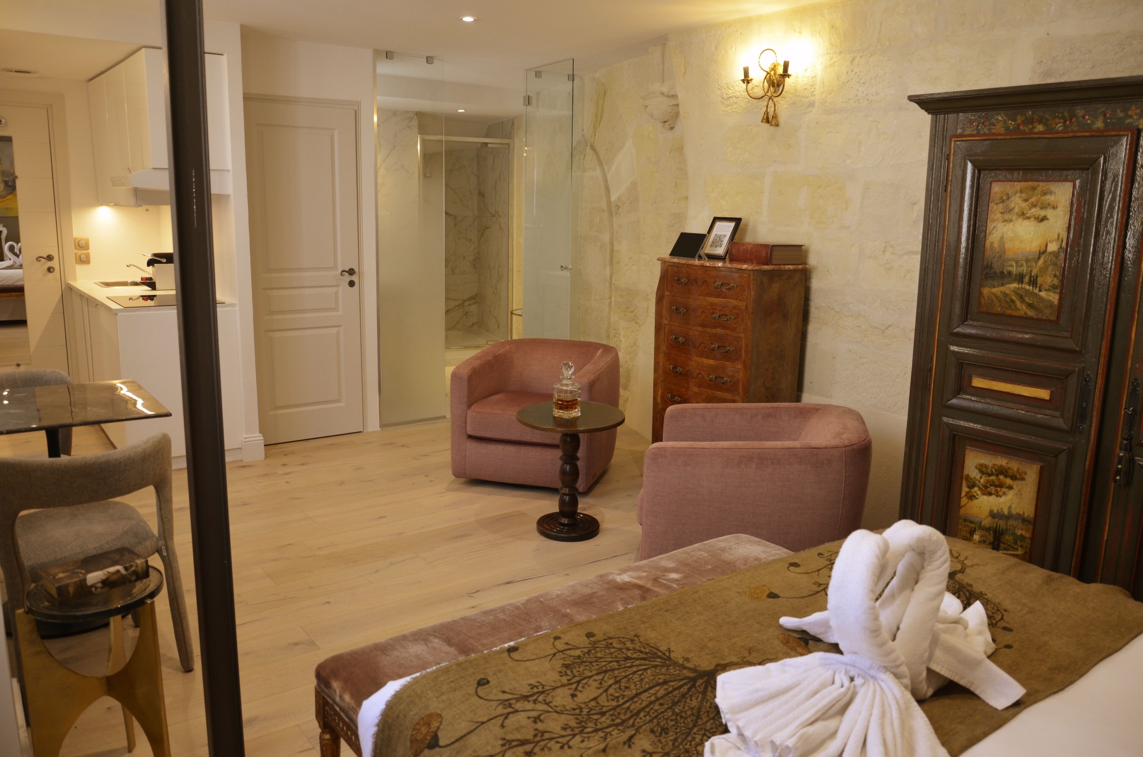 Habitación de hotel con cama, zona de estar con una silla y una mesita, armario y baño visible a través de una puerta abierta.