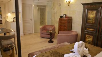 Habitación de hotel con cama, zona de estar con una silla y una mesita, armario y baño visible a través de una puerta abierta.