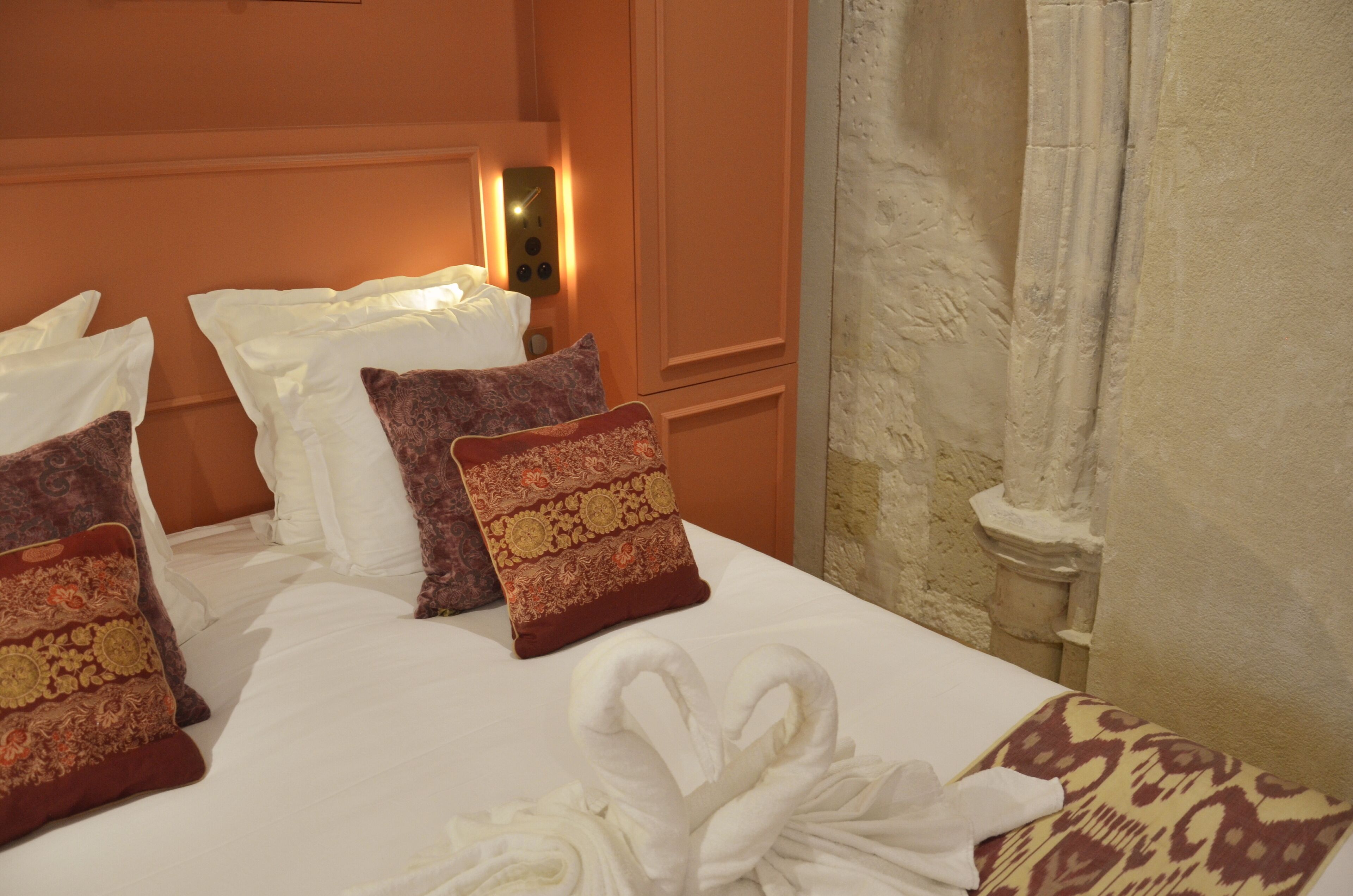 A hotel room with a neatly made bed, a wall-mounted light, and a curtain.