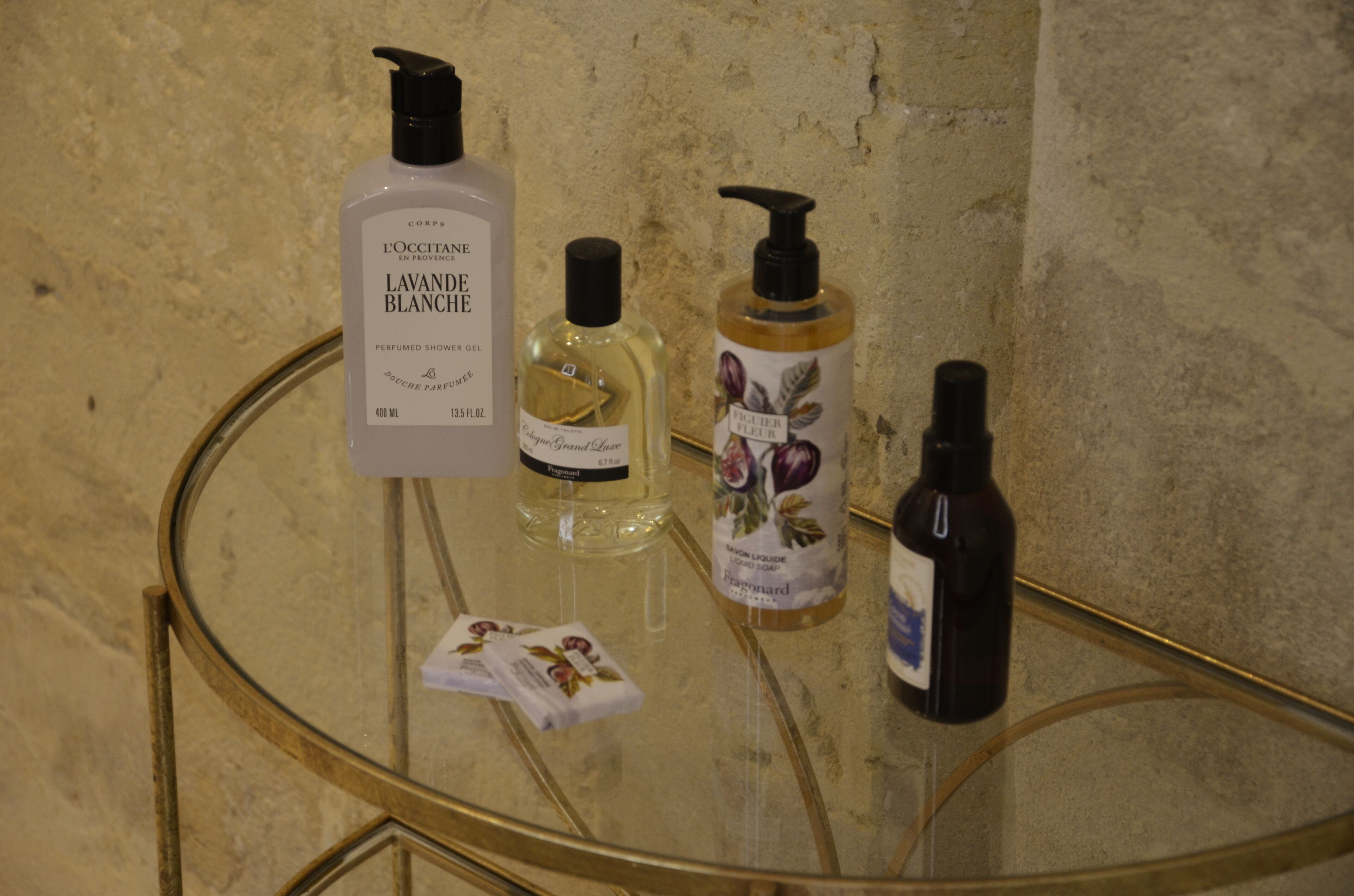 Une table en verre sur laquelle sont posées trois bouteilles de parfum et un paquet de mouchoirs.