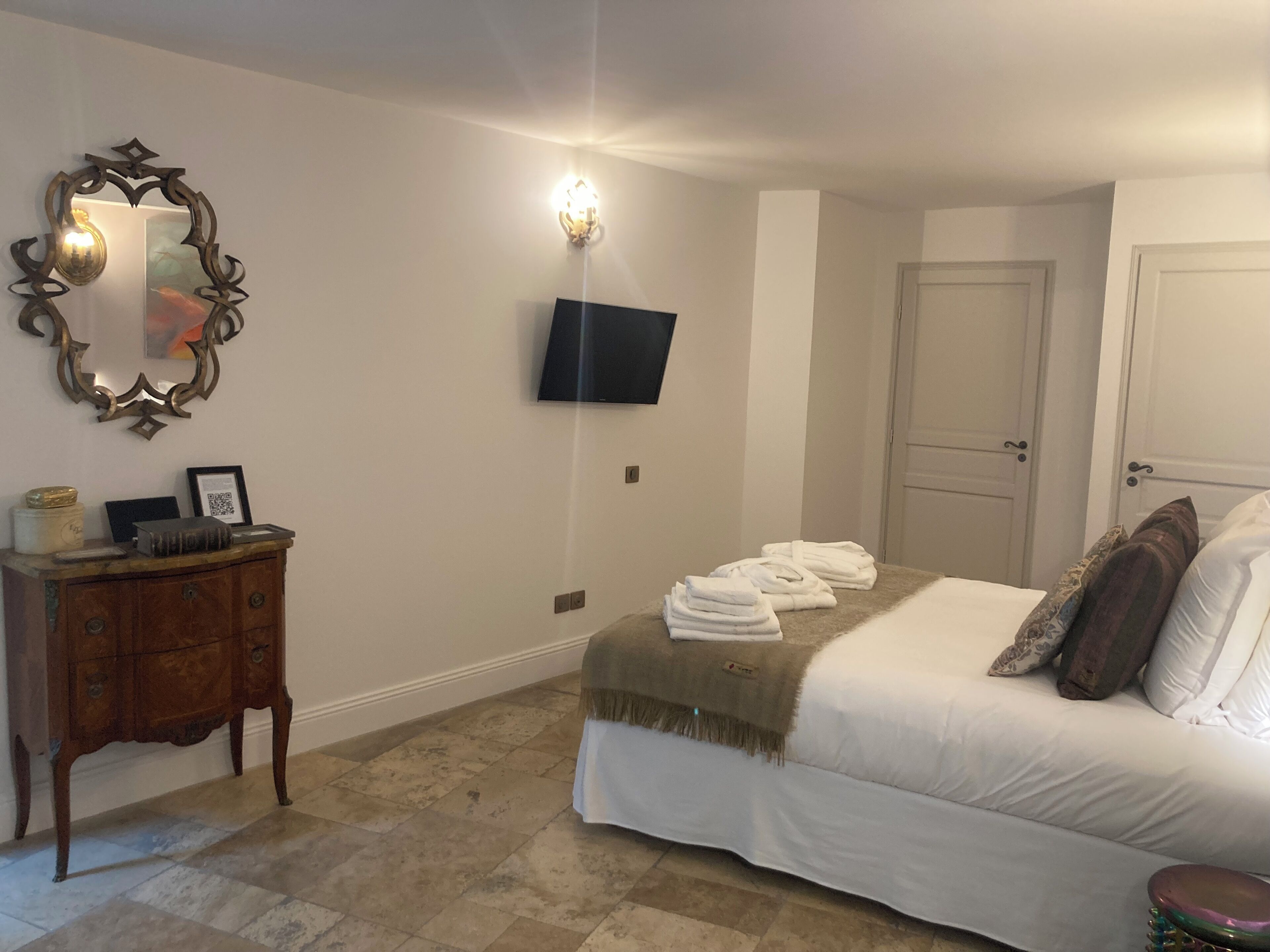 Un dormitorio con cama, cómoda, espejo, televisor montado en la pared y una puerta.