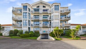 Un immeuble résidentiel à plusieurs étages, doté de balcons, d’une entrée sécurisée et d’un aménagement paysager bien entretenu.