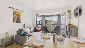 Un salon moderne comprenant un coin repas, un canapé, une table basse et offrant une vue sur la ville grâce à de grandes fenêtres.