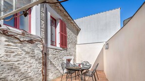 A small outdoor patio with a table and chairs, a stone wall, and a window with red shutters. - Close to port & beaches - Terrace - House for 5 (Pornic)