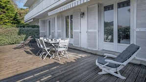 Un'area esterna coperta con un pavimento in legno, un tavolo con sedie e una poltrona da relax.