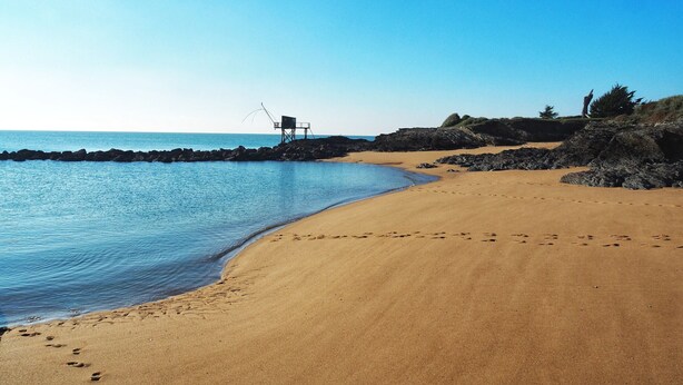 Una spiaggia con un litorale roccioso, una torretta per i bagnini e impronte sulla sabbia.