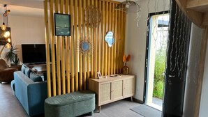 A modern living room with a sectional sofa, a small bench, a wooden cabinet, and a TV. - 3-bedroom house with garden in Arès, 500m from beach and lake (Arès)