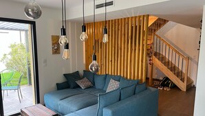 A modern living room with a blue sectional sofa, hanging light bulbs, and a wooden slat wall. - 3-bedroom house with garden in Arès, 500m from beach and lake (Arès)