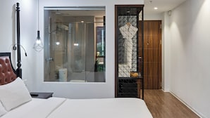 A modern bedroom with a large bed, a glass shower enclosure, a wooden wardrobe, and a small window.