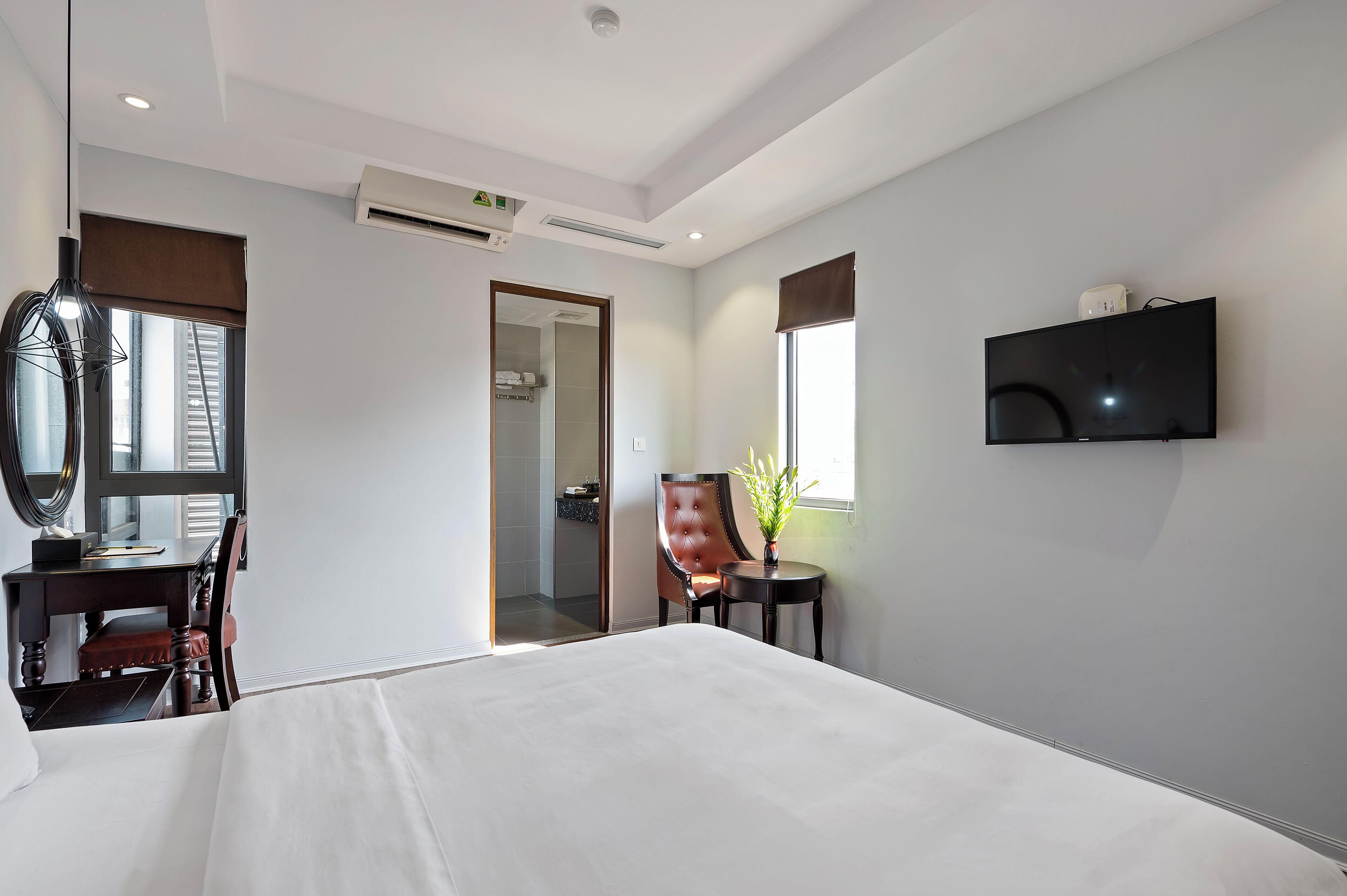 A hotel room with a large bed, a desk with a chair, a television mounted on the wall, and a window with a view of the outside.