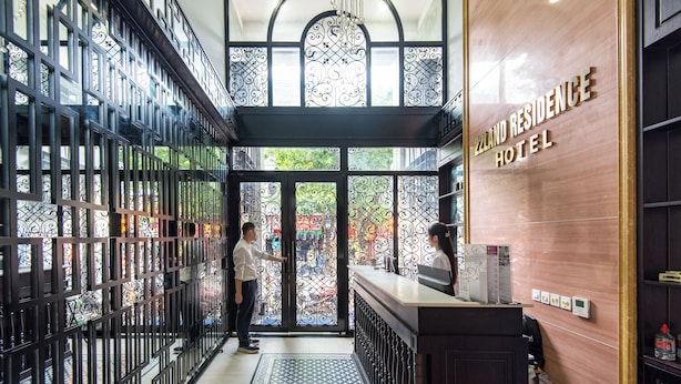 A reception area with a modern design, featuring a reception desk, a decorative glass door, and a sign for the Zeland Residence Hotel.
