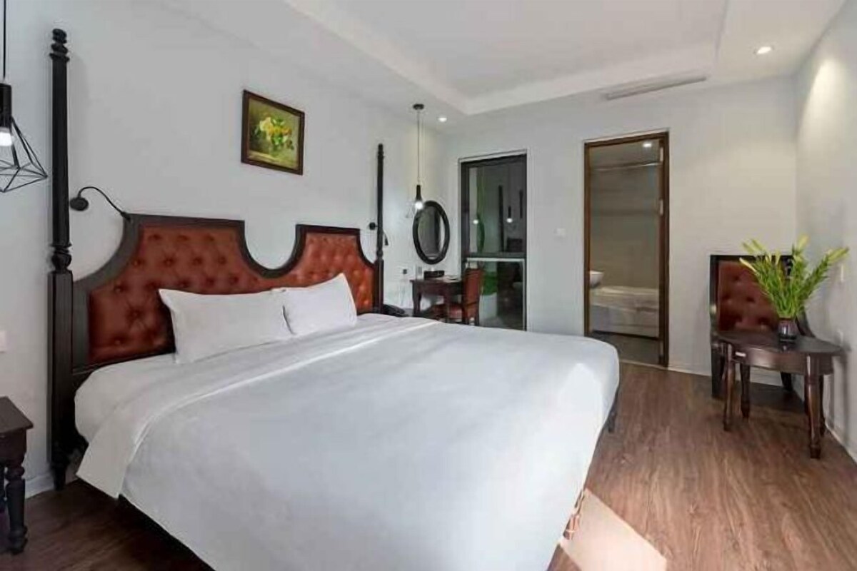 Une chambre d’hôtel avec un grand lit, une tête de lit en bois, une table de chevet et une petite plante en pot.