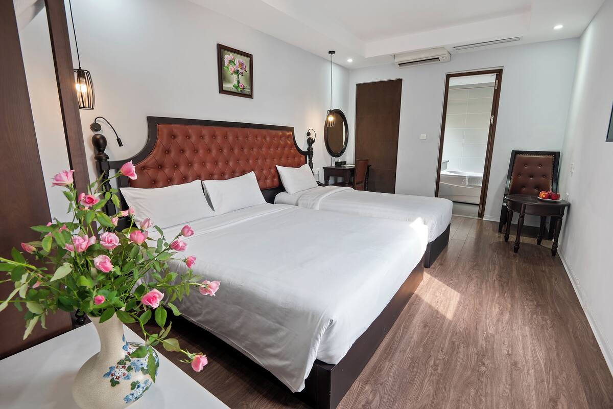 A hotel room with a large bed, a bedside table with a vase of flowers, a chair, and a mirror.