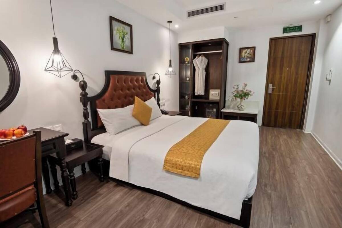 A hotel room with a bed, bedside table, lamp, wardrobe, and a mirror.