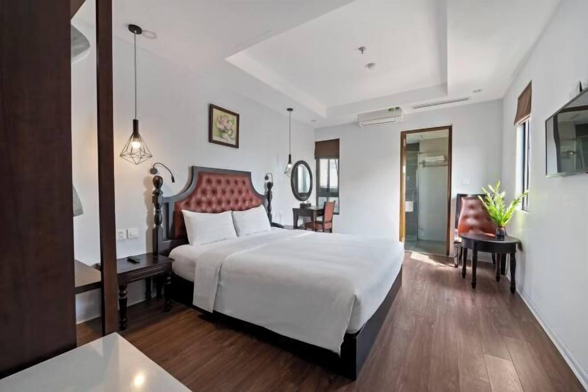 A hotel room with a large bed, a bedside table, a chair, a mirror, a potted plant, and a TV on the wall.